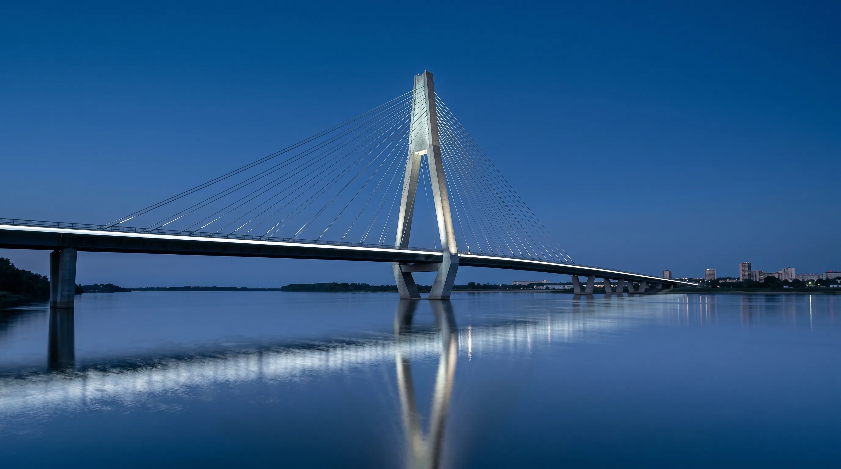 A cable-stayed bridge lit over the river at dusk, the light landing on the structure rather than aimed at the sky