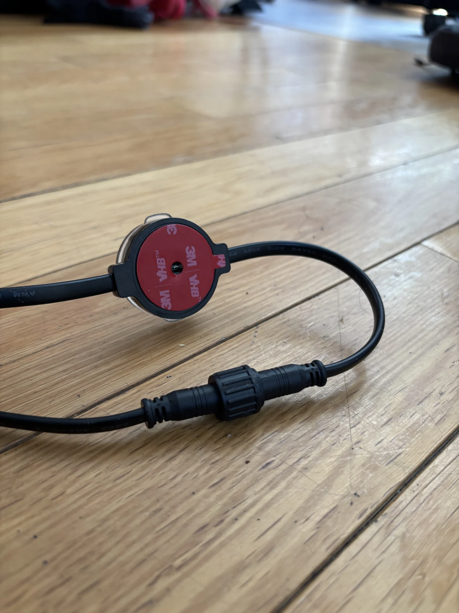 Un point lumineux vu de dos, sa pastille de ruban double face rouge intacte, à côté d’un connecteur étanche