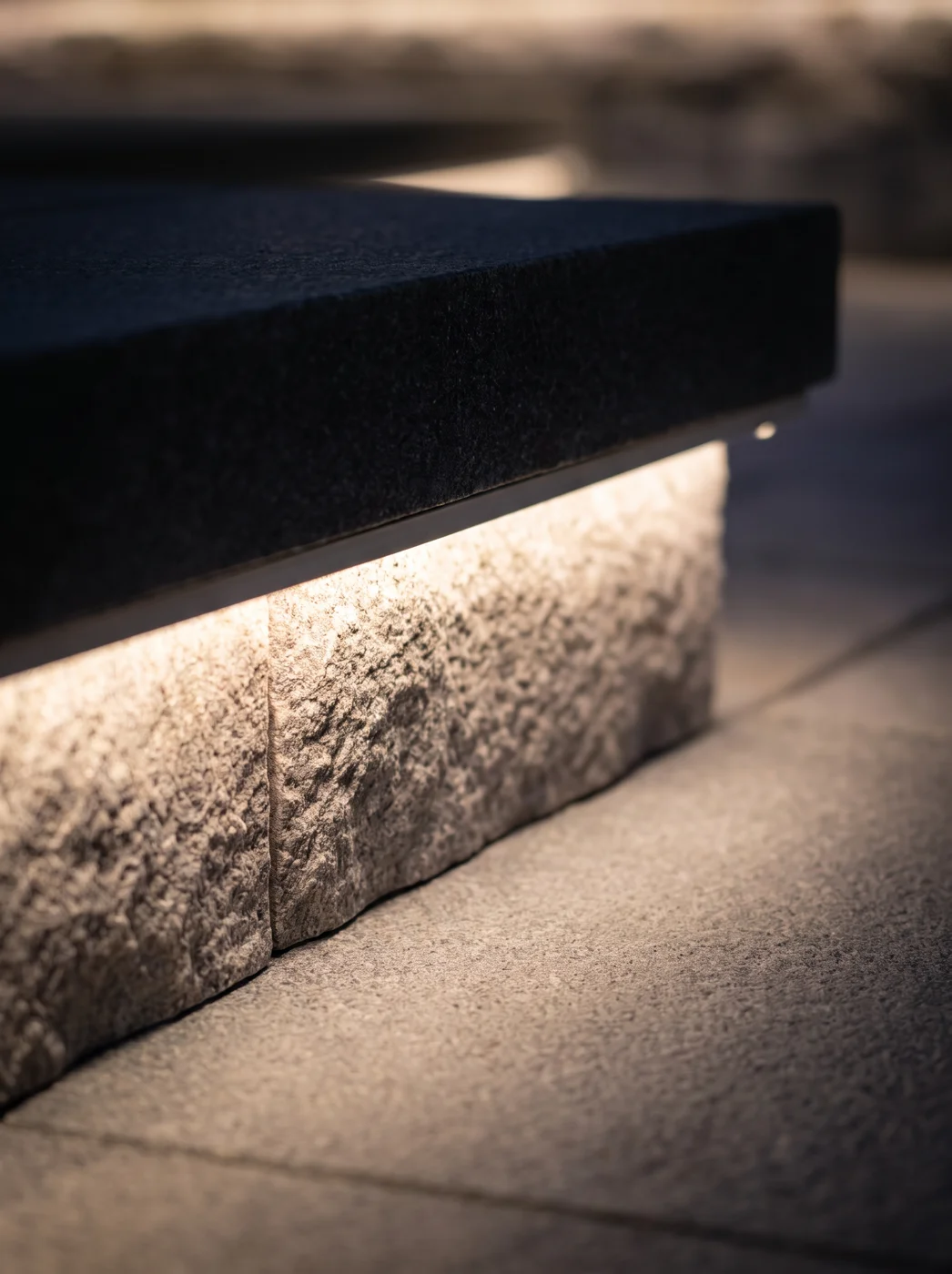 Warm-white LED tucked under the nose of a stone step, washing light down onto the riser below — no fixture visible