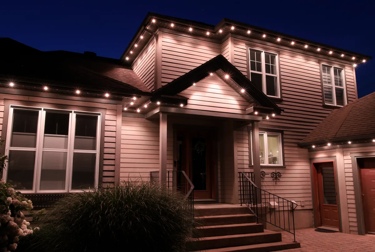A two-storey home at dusk with warm white LED lights along the entire roofline and gable peaks, illuminating a covered entry