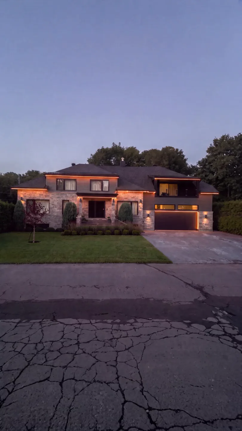 A two-storey stone and siding home at dusk with its roofline, entry and garage picked out in warm white permanent LED
