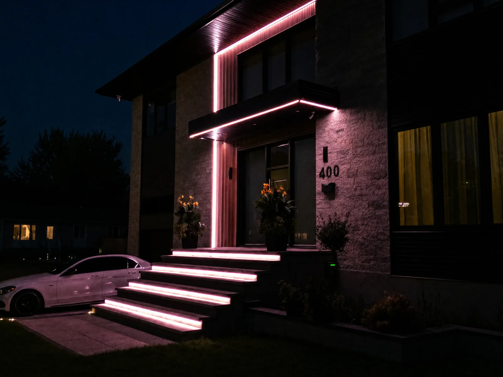 Modern home entrance at night with pink permanent RGB LED tracing the door canopy and recessed into each front step — a Québec install